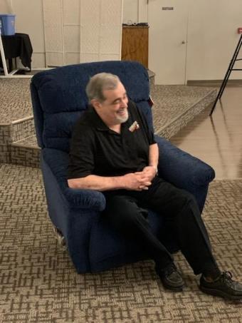Dr. Neil Sass smiling as he sits in his new rocking chair.